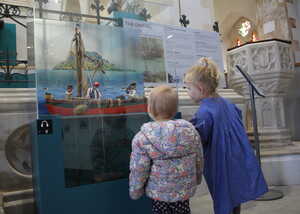 Two children observe a historical ship display in a museum setting.