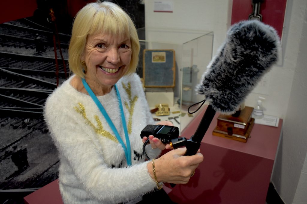 A female volunteer holding a furry boom mike and a recording device