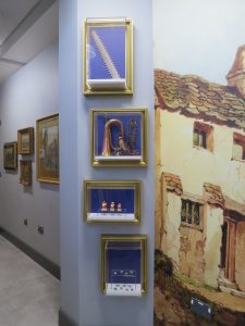As you walk into the museum (or pop to the loo) you are greeted by a painting of Newton Abbot printed on the wall, along with an eclectic group of objects. These objects don’t have labels as we wanted to inspire you to come in and look at all our other objects. But if you’re curiosity was piqued, you’re in the right place. This slideshow takes you through the story of the four framed items.