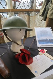 The ceramic poppy beneath the helmet is one of 888,246 created as part of the art installation Blood Swept Lands and Seas of Red. In 2014 they were displayed at the Tower of London to commemorate the centenary of WW1. Each poppy represented a British serviceman who lost their life in the conflict.
