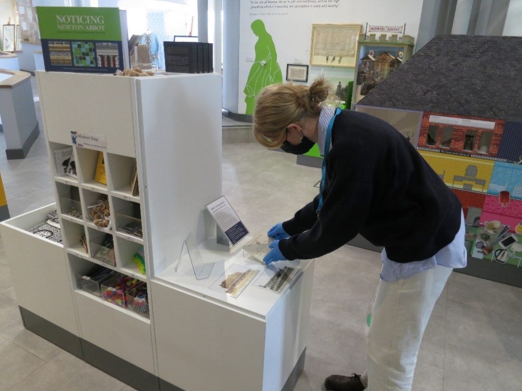 Woman wearing gloves and a mask placing a museum object inside a display case
