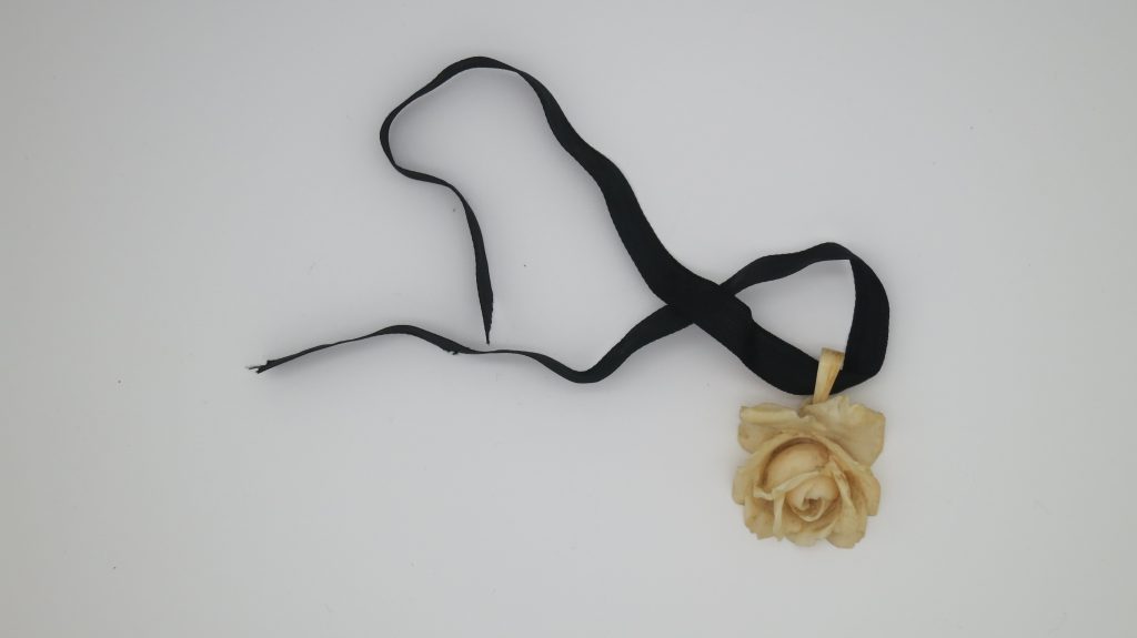 A cream rose pendant made of ivory attached to a black ribbon (Victorian)