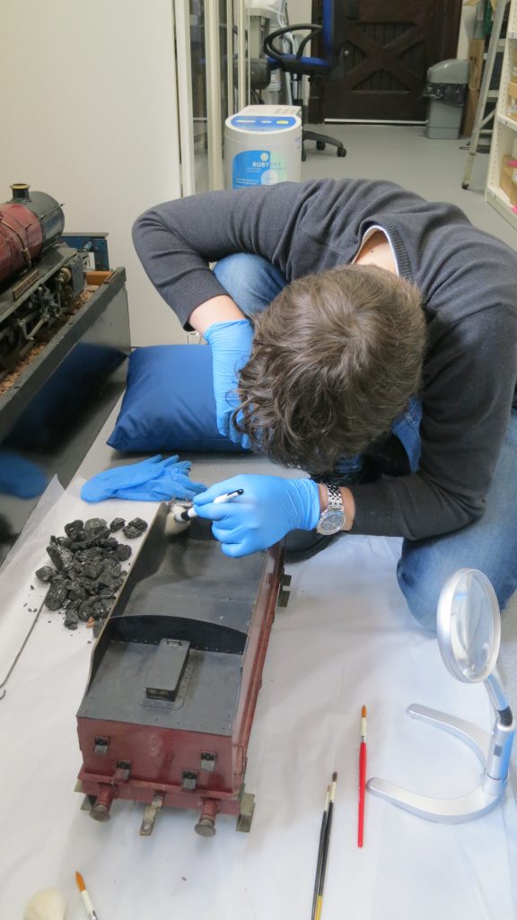 Young man wearing blue protective gloves uses a brush to clean a model locomotive