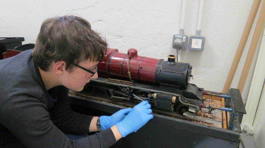 Young man with glasses and blue nitrile gloves cleaning a red model locomotive