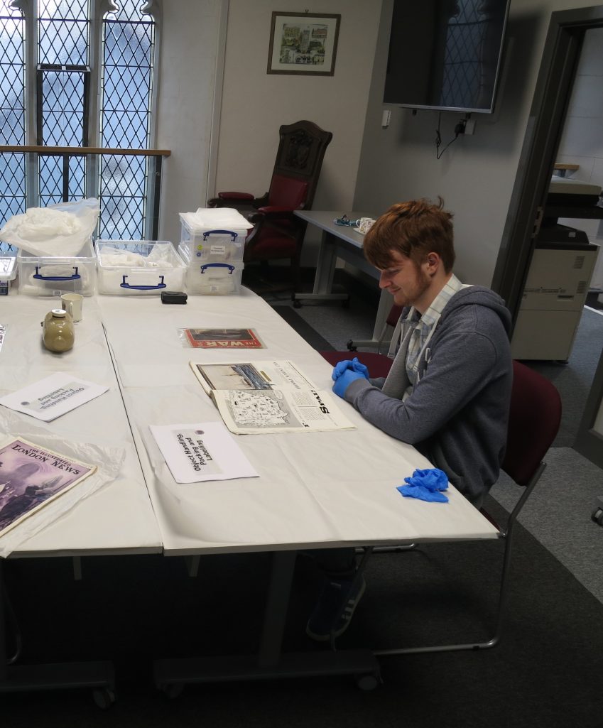 Man sat a desk wearing protective gloves looking a historical papers