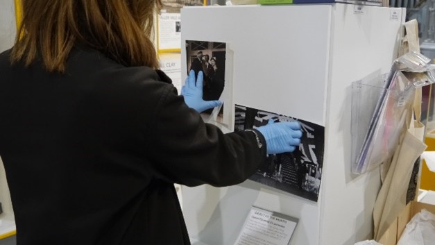 A work experience student placing copies of photographs at the back of a display case, helping to design the display